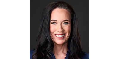 Portrait of a smiling faculty member with long dark hair against a dark studio background.
